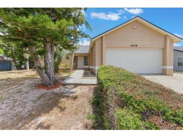 Tan single-story home featuring an attached garage, well-kept shrubs, and mature landscaping at 2838 Maldive Ct, Deltona, FL 32738