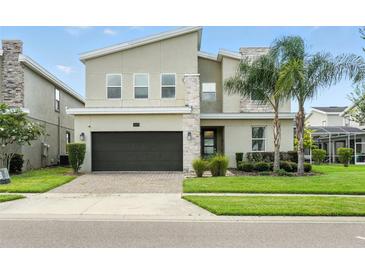 Charming two-story home featuring stone accents, a two-car garage, and a well-manicured lawn with palm trees at 369 Ocean Course Ave, Davenport, FL 33896