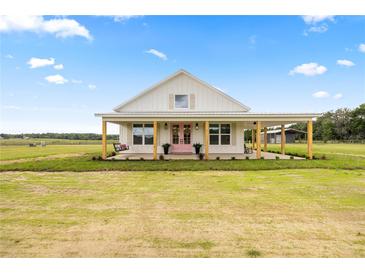 Charming farmhouse with a large front porch, pink doors, and a beautifully maintained lawn at 22212 Sw 210Th Ave, Dunnellon, FL 34431