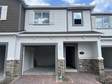 Two-story townhome with stone accents, light gray siding, an open garage and front door at 5087 Prairie Preserve Run, St Cloud, FL 34772