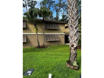 Exterior view of tan two-story building with well-manicured lawn and tropical landscaping at 120 Hibiscus Woods Ct # 11B, Deltona, FL 32725