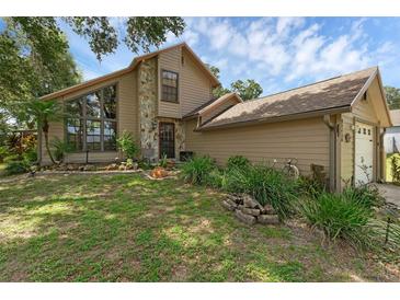 Charming tan home featuring a stone facade, large windows, mature landscaping, and an attached garage at 25438 Pine Valley Dr, Sorrento, FL 32776
