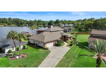 Expansive lakefront home with manicured lawn, mature palms, and a long driveway leading to an attached garage at 3604 Shell Cove Ln, Orlando, FL 32817