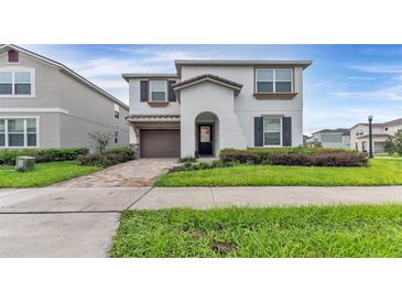 Two-story home with a well-manicured lawn, brick driveway, and stucco exterior at 2114 Fleming Mist Pl, Kissimmee, FL 34747