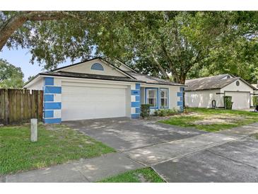 Charming one-story home featuring blue and white accents, a two-car garage, and mature landscaping at 4398 Fox Hollow Cir, Casselberry, FL 32707