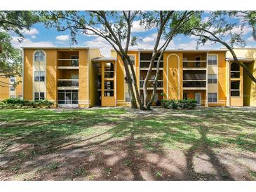Inviting yellow apartment building with mature trees and well-maintained green lawn under a blue sky at 5263 Images Cir # 306, Kissimmee, FL 34746
