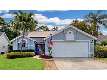 Charming single-Gathering home featuring a manicured lawn, mature palm trees, and a two-car garage with an American flag at 14529 Falling Tree Ct, Orlando, FL 32837