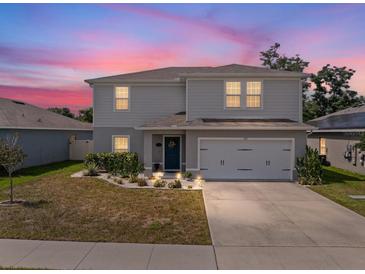 Two-story home featuring a gray exterior, two-car garage, and a manicured lawn at 253 Fiddlewood Ct, Davenport, FL 33837