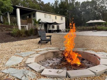 Outdoor fire pit and chairs on gravel; lush greenery and modern white home in the background at 610 Cypress Ave, Orange City, FL 32763