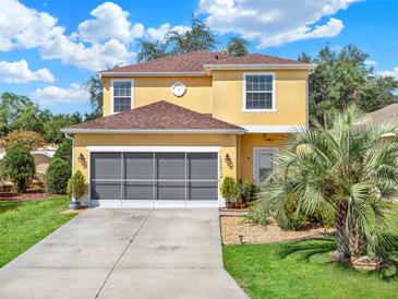 Inviting two-story home featuring a well-manicured lawn, grey garage door, and lush landscaping at 12347 Ne 52Nd Loop, Oxford, FL 34484