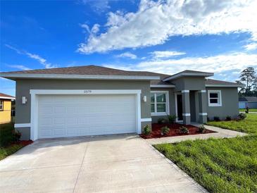 Charming single-story home featuring a two-car garage, gray stucco, manicured landscaping, and a concrete driveway at 2579 Sw 146Th St, Ocala, FL 34473
