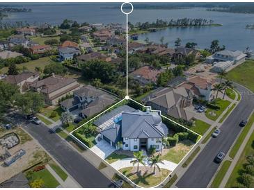 Aerial view of a luxury home with a blue roof, circular driveway, and stunning lake views at 5708 Emerington Cres, Orlando, FL 32819