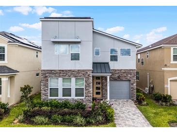 Modern two-story home featuring a stone facade, gray siding, a paved driveway, and manicured landscaping at 8913 Coconut Breeze Dr, Kissimmee, FL 34747