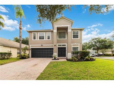 Two-story home features a dark garage door, manicured lawn, and brick paver driveway on a sunny day at 9067 Stonebury Way, Orlando, FL 32832