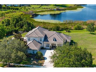 Stunning aerial view of a grand home with a tile roof, mature trees, and a tranquil lake backdrop at 13025 Lake Roper Ct, Windermere, FL 34786