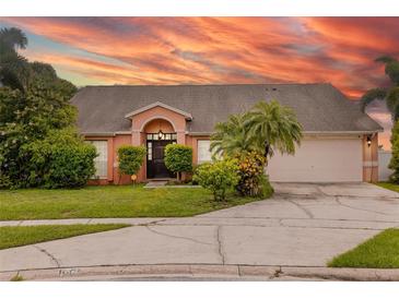 Inviting single-story home featuring a two-car garage, beautifully landscaped yard, and a striking pink exterior at sunset at 1606 Burryport Dr, Orlando, FL 32837