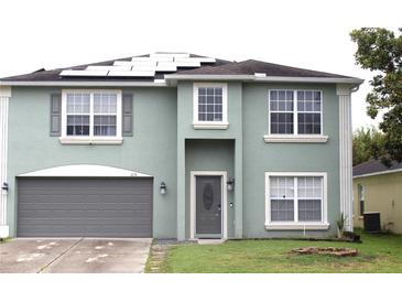 Two-story home featuring a gray front door, a two-car garage, solar panels and manicured green lawn at 115 Willowbay Ridge St, Sanford, FL 32771