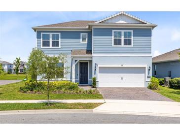 Two-story home featuring blue siding, a well-manicured lawn, and a two-car garage with a brick-paved driveway at 13829 Destin Beach Ln, Orlando, FL 32827