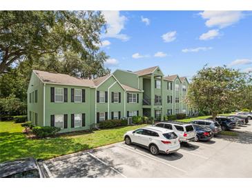Green apartment building with black shutters, a well-manicured lawn, and ample parking on a sunny day at 2035 Dixie Belle Dr # 2035C, Orlando, FL 32812