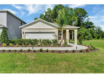 Charming single-story home features a manicured lawn and a two-car garage with mature trees in the background at 2888 House Finch Rd, St Cloud, FL 34773