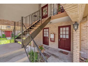 A welcoming apartment exterior featuring red doors, brick accents, and stairwell to the second level at 200 St Andrews Blvd # 802, Winter Park, FL 32792