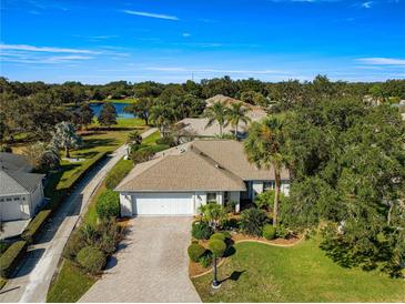 Beautiful single-story home with a two-car garage, brick driveway, mature trees and landscaping, and partial lake view at 7290 Se 172Nd Legacy Ln, The Villages, FL 32162