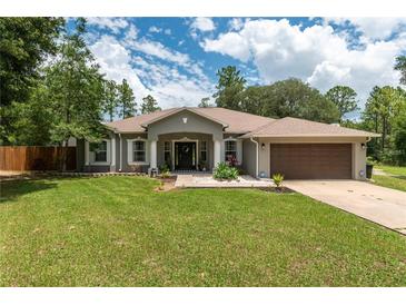 Charming single-story home featuring a manicured lawn, lush landscaping, and attached two-car garage at 12805 Sw 64Th Ln, Ocala, FL 34481