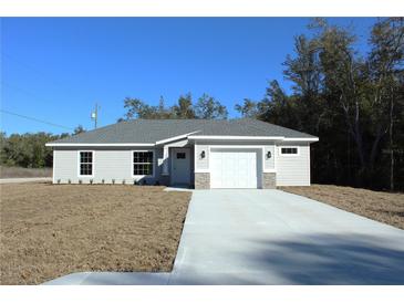 One-story house with gray siding, white garage door, and a stone accent at 13441 Sw 113Th Pl, Dunnellon, FL 34432