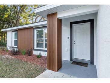 Charming single-story home featuring a white front door and modern wood-accented entry way with beautiful landscaping at 13573 Sw 115 Pl, Dunnellon, FL 34432