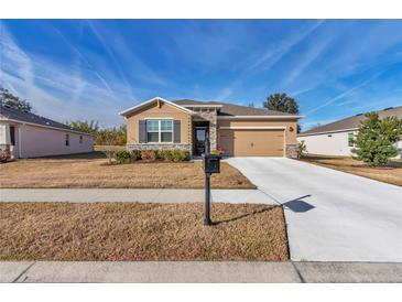 Tan house with stone accents, two-car garage, and landscaped yard at 6365 Sw 88Th Loop, Ocala, FL 34476