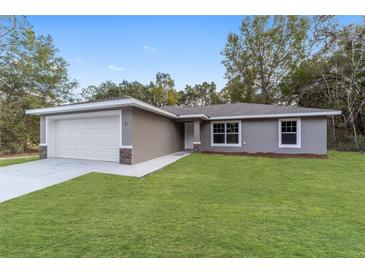 Newly constructed home with a gray exterior, attached garage, and well-manicured lawn at 24268 Sw Tiger Lake W Blvd, Dunnellon, FL 34431