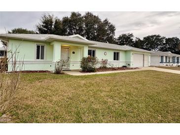 Light green single story home with a two car garage and well manicured lawn at 6184 Sw 101St Pl, Ocala, FL 34476