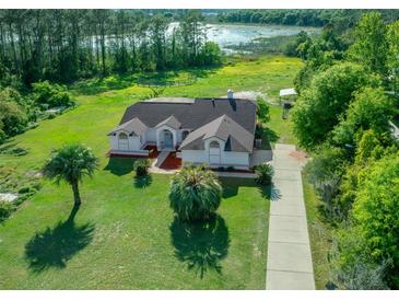 Aerial view of a single-story home with a large yard, long driveway and lake view at 11540 Se Highway 464, Ocklawaha, FL 32179