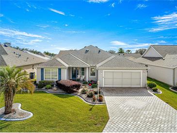 Single-story home with landscaped yard, paver driveway, and two-car garage at 1918 Walden Way, The Villages, FL 32162