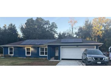 Blue house with solar panels and a white garage door at 6701 Se 122Nd Ln, Belleview, FL 34420
