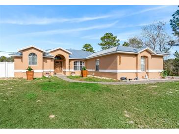 Tan house with gray metal roof, walkway, and landscaping at 22287 Sw Mango Ln, Dunnellon, FL 34431