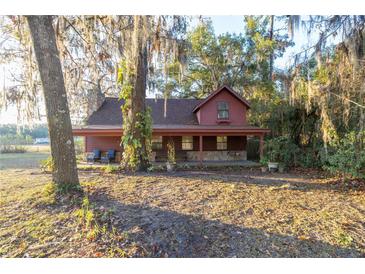 Rustic red house with covered porch sits on a grassy lot, surrounded by large trees at 876 Ne 71St Ln, Ocala, FL 34479