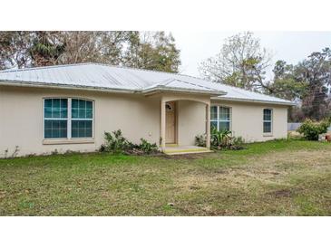 Beige house with metal roof, light brown door, and green lawn at 70 Se 81St Pl, Ocala, FL 34480