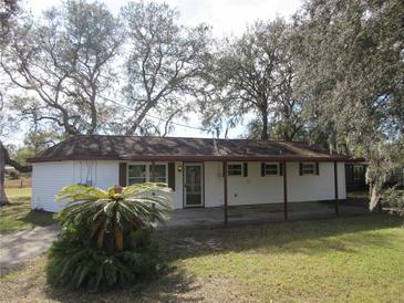 White house with covered patio, mature landscaping, and a large yard at 18782 Se 50Th St, Ocklawaha, FL 32179