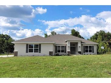 Single-story home with a light-colored facade, dark roof, and neatly landscaped lawn at 5322 Sw 137Th Ct, Ocala, FL 34481