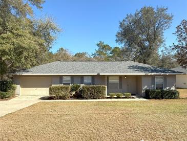 Beige house with gray roof, attached garage, and landscaping at 73 Fir Dr, Ocala, FL 34472