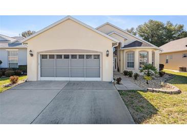 Tan one-story house with gray garage door, landscaping, and walkway at 6760 Sw 112Th St, Ocala, FL 34476