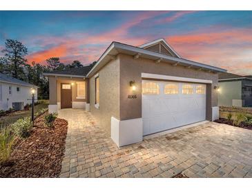 Charming exterior showcasing a manicured lawn and a two-car garage with a brick-paved driveway, under a vibrant twilight sky at 10306 Sw 99Th Ln, Ocala, FL 34481