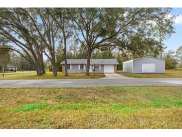 Charming single-story home featuring mature trees, gray stucco siding, and an attached one car garage at 26 Spring Cir, Ocala, FL 34472