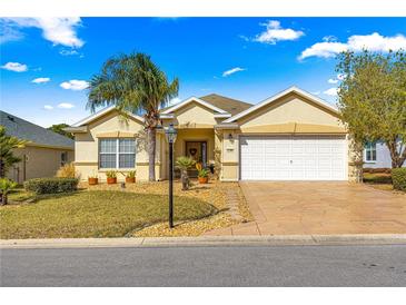 Charming one-story home with a well-manicured lawn, a palm tree and a two-car garage at 12595 Se 97Th Terrace Rd, Summerfield, FL 34491