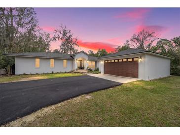 Beautiful single-story home featuring a paved driveway, manicured lawn and mature trees under a pink and purple sky at 1610 Se 22Nd Ave, Ocala, FL 34471