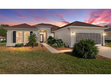 Charming single-story home featuring a well-maintained lawn, mature landscaping, and a two-car garage under a beautiful sunset sky at 13187 Se 93Rd Terrace Rd, Summerfield, FL 34491