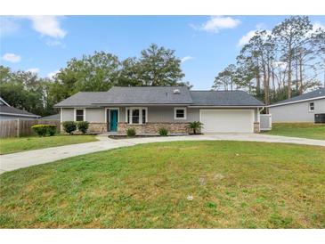 Charming home featuring a teal door, well-manicured lawn, and an attached two car garage at 6 Cherry Drive Ln, Ocala, FL 34472