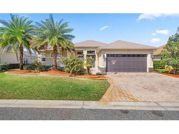 Beautiful home featuring a two-car garage, manicured lawn, mature palm trees, and brick-paved driveway at 10138 Lake Miona Way, Oxford, FL 34484