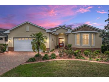 Charming single-story home with manicured landscaping and a brick-paved driveway, complemented by a warm sunset at 9274 Sw 94Th Loop, Ocala, FL 34481